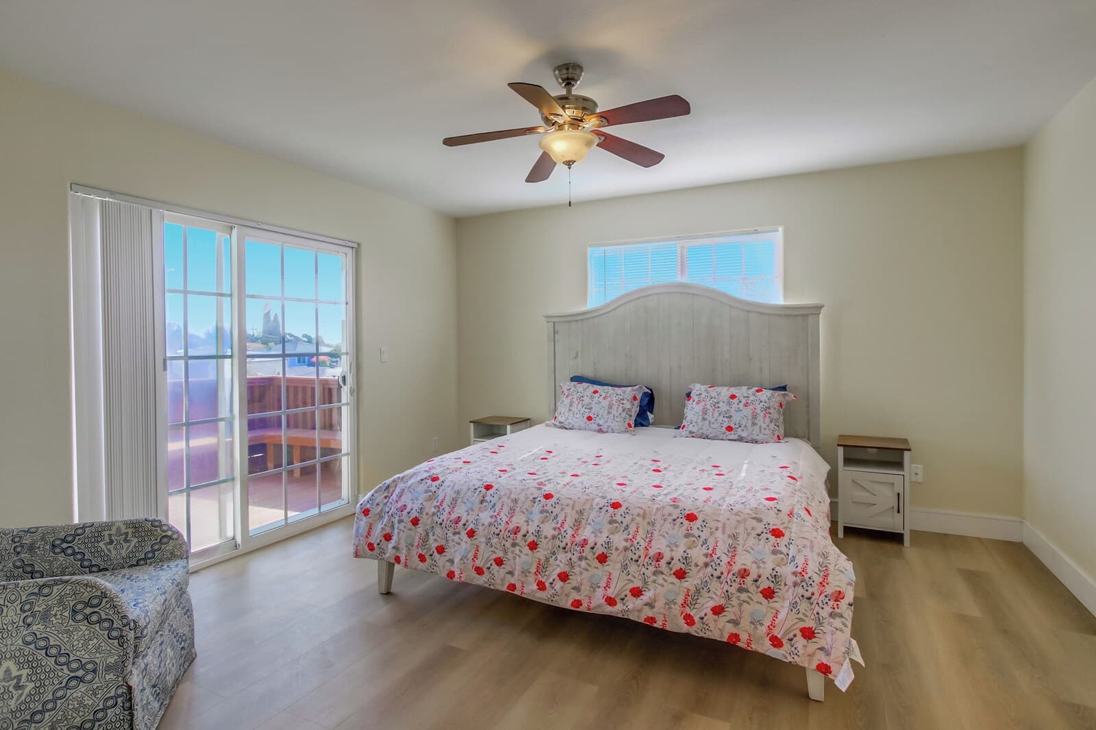 A bedroom with a bed, a ceiling fan, a nightstand, a chair, and a window with blinds.