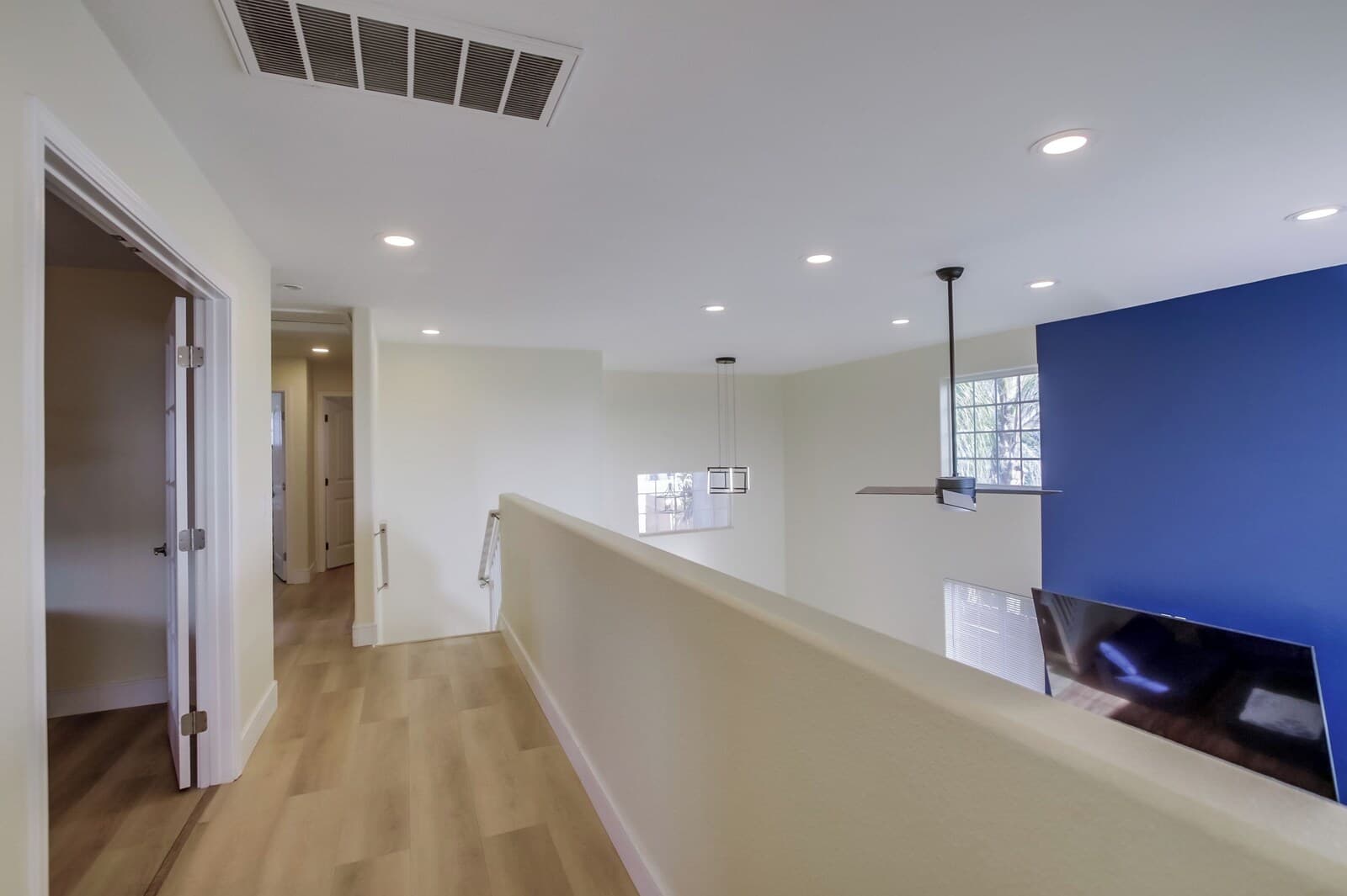 A hallway with a wooden floor, white walls, and a blue accent wall. There is a door on the left and a window on the right.
