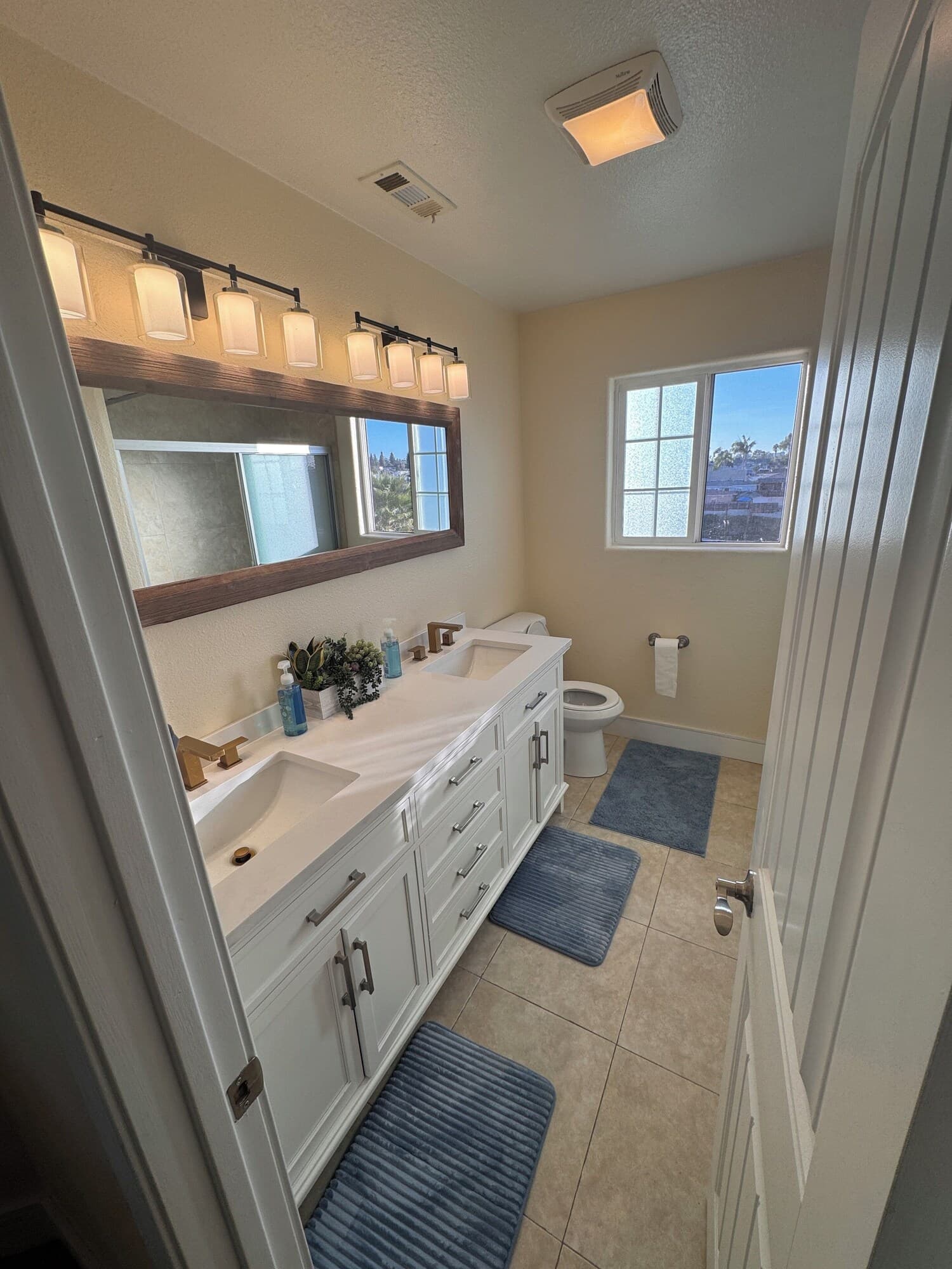A modern bathroom with a double sink vanity, a large mirror, and a window providing a view of the outside.