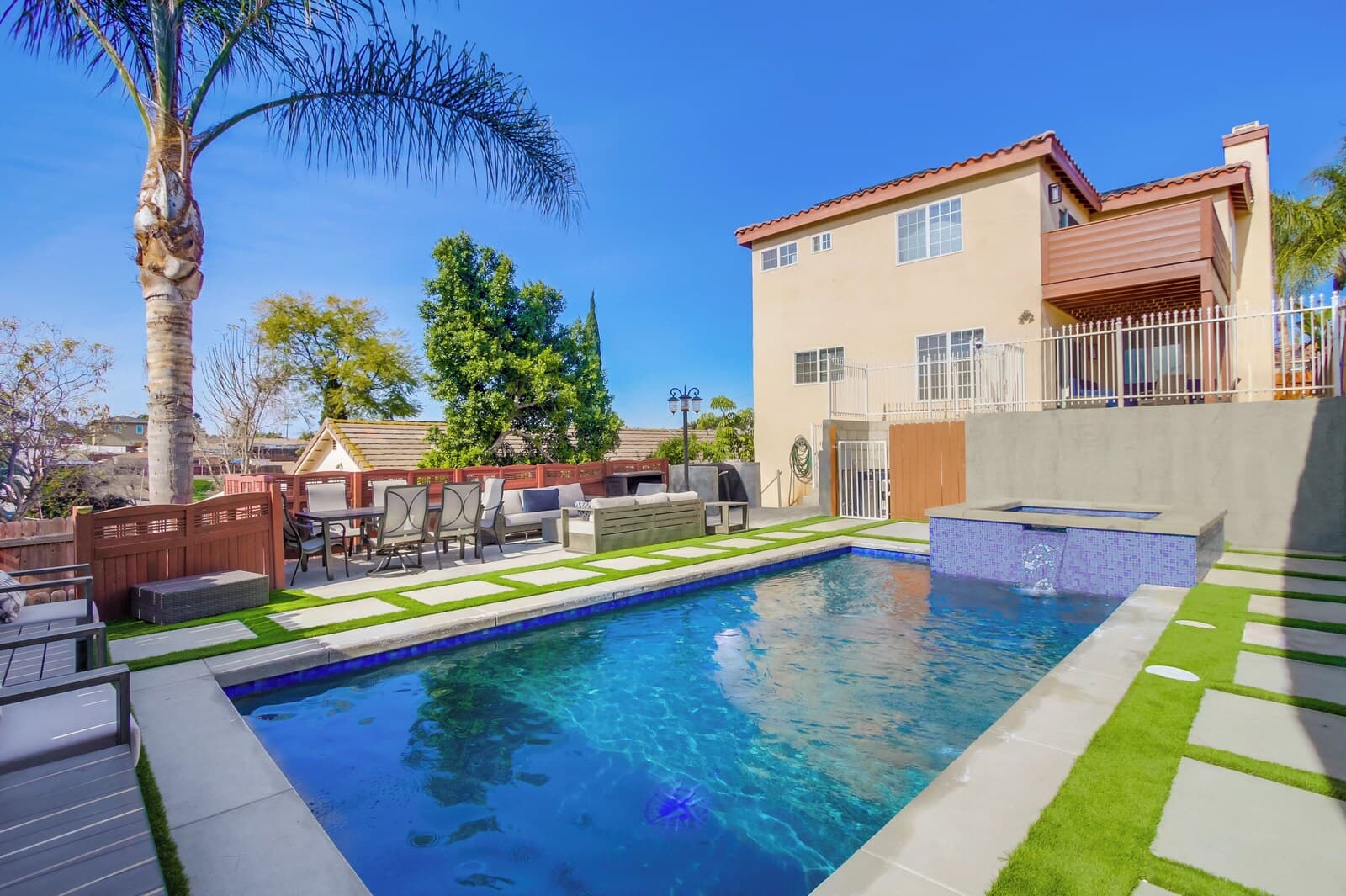 A backyard with a swimming pool, patio furniture, and a two-story house.