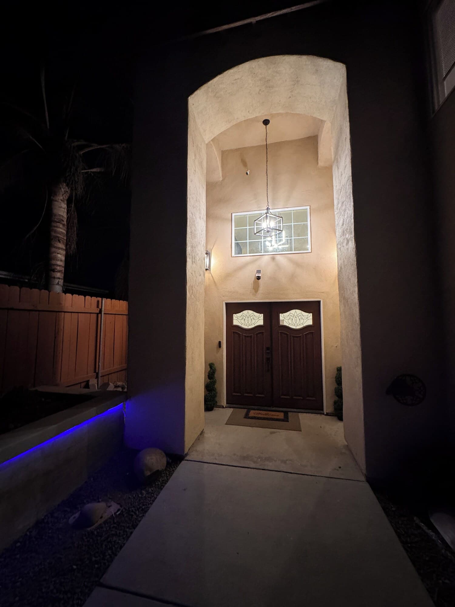 A modern entrance with a concrete archway, a glass door with a geometric design, and a hanging light fixture.