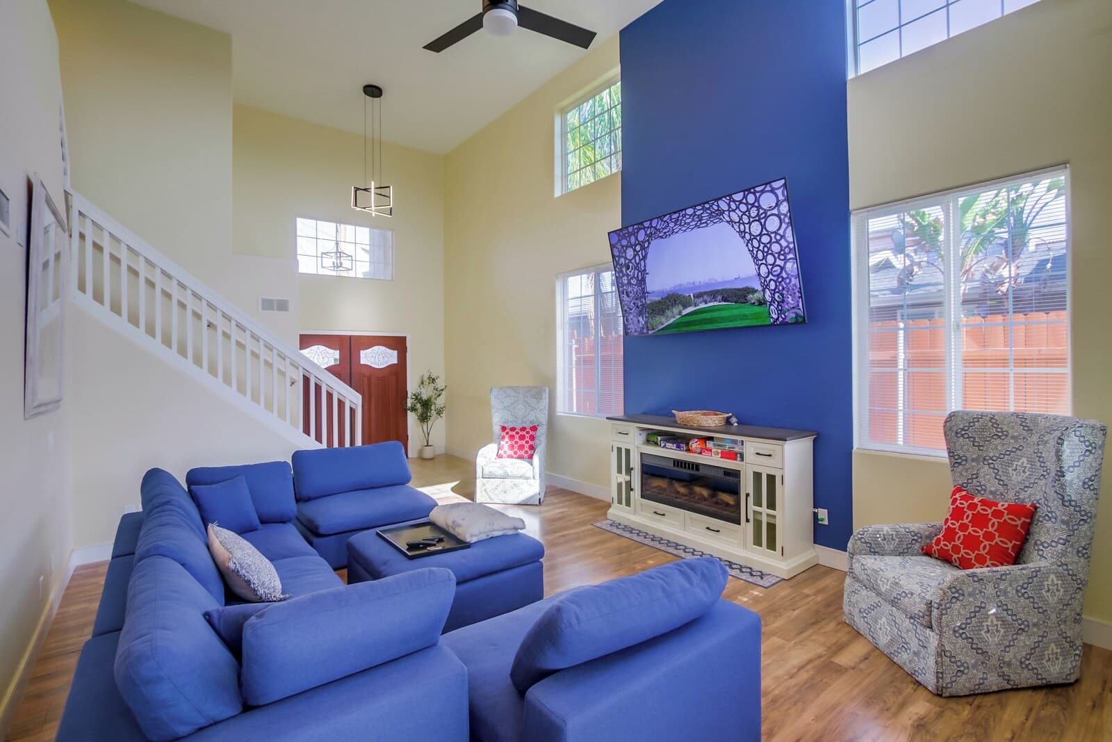 A spacious living room with a blue sectional sofa, a grey patterned armchair, and a television mounted on the wall.