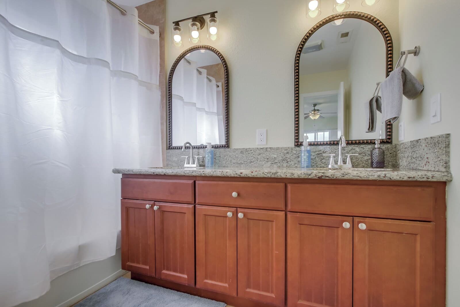 A bathroom with wooden cabinets, a granite countertop, a large mirror, and a shower curtain.