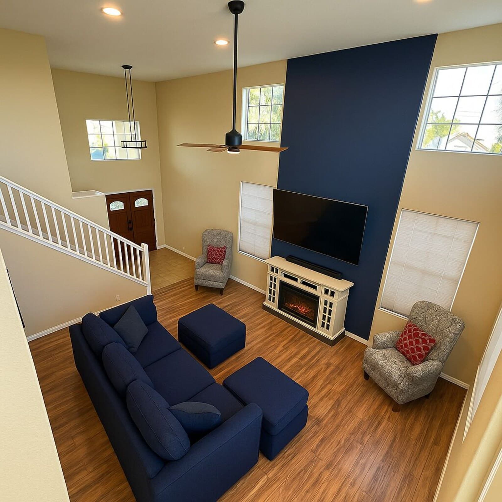 A living room with a sectional sofa, ottomans, a flat-screen TV, a fireplace, and a staircase.