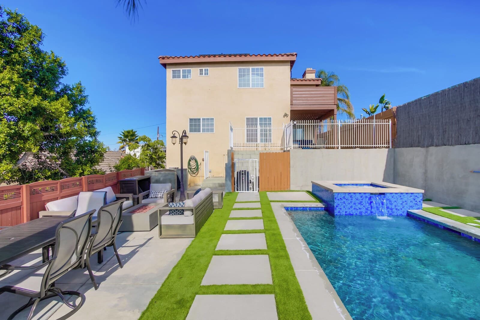 A backyard with a swimming pool, outdoor seating, and a two-story house.