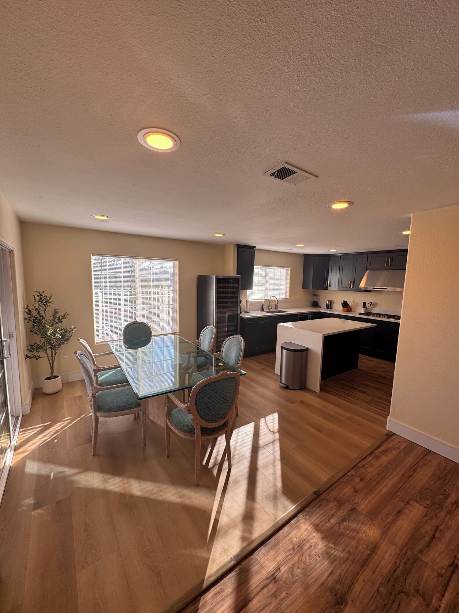A modern kitchen with a dining area, wooden flooring, and a view of the city.