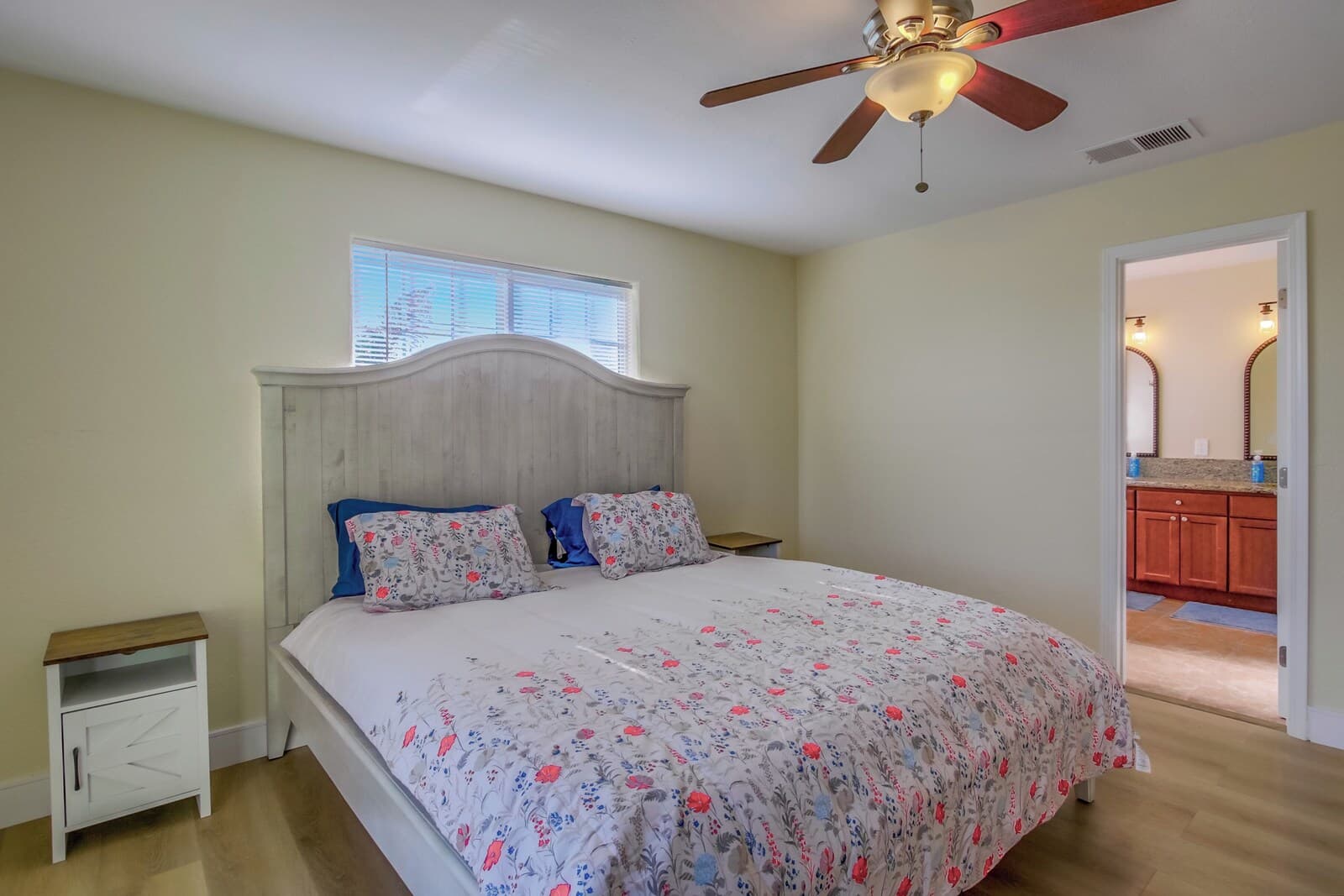 A bedroom with a bed, a nightstand, a ceiling fan, and a window.