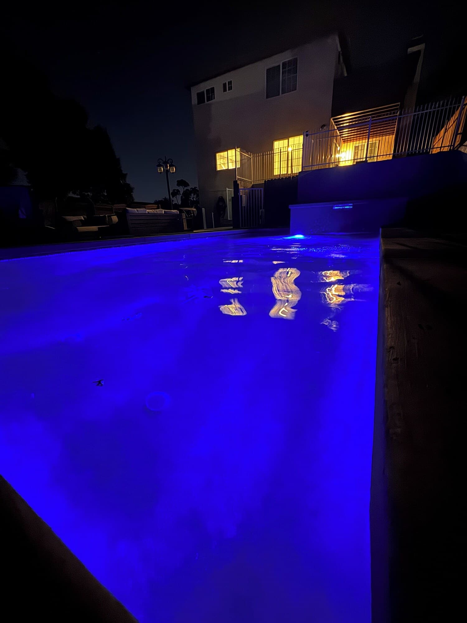 A swimming pool with blue lighting at night, surrounded by a building with illuminated windows.