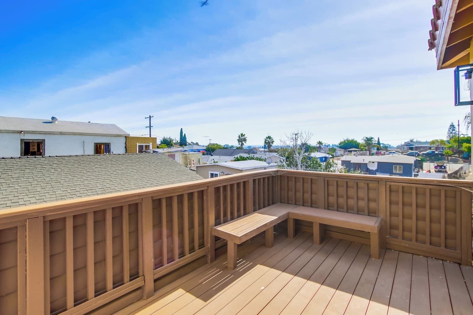 A wooden deck with a bench, overlooking a residential area with houses and a clear sky.