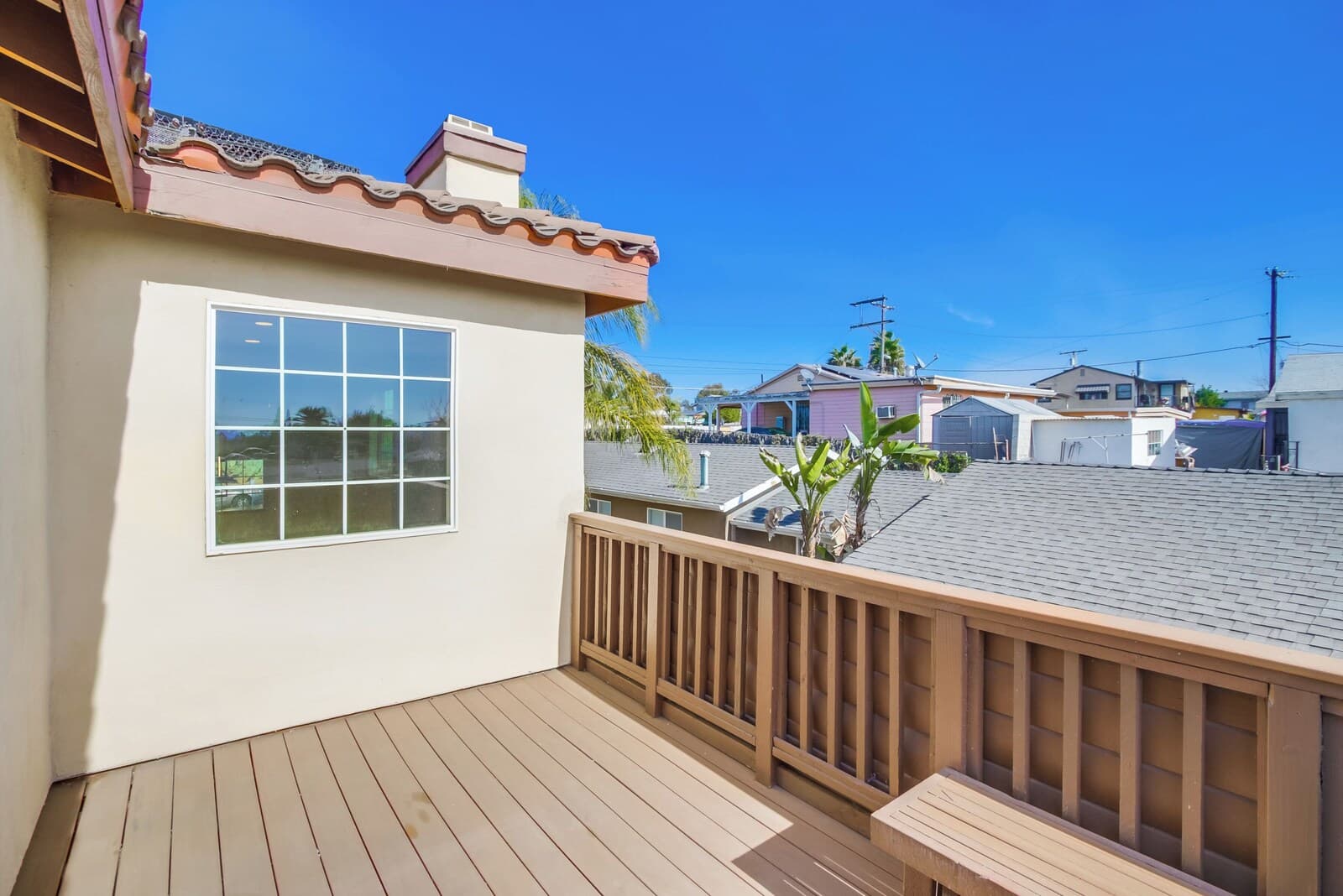 A wooden deck with a view of neighboring houses and a clear blue sky.